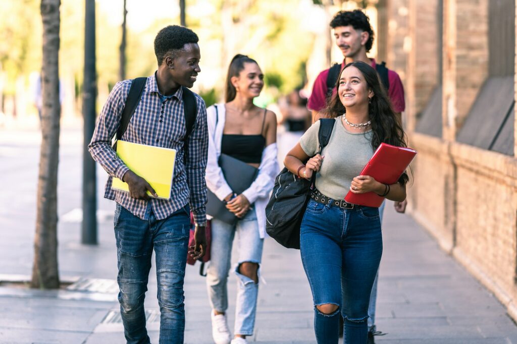 Four students of different ethnicities walking in outdoors with school material